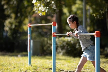 Photo for Girl playing horizontal bar in autumn park - Royalty Free Image