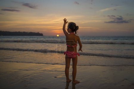 Téléchargez les photos : Petite fille agitant la main au coucher du soleil - en image libre de droit