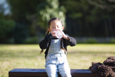 Téléchargez les photos : Petite fille boire de l'eau dans le parc - en image libre de droit