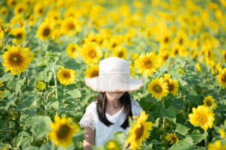 Téléchargez les photos : Une fille portant un chapeau jouant dans un champ de tournesol - en image libre de droit