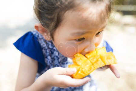 Téléchargez les photos : Bonne petite fille mangeant de la mangue - en image libre de droit