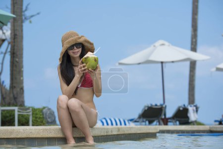 Téléchargez les photos : Belle japonaise femme boire du jus de noix de coco sur le bord de la piscine - en image libre de droit