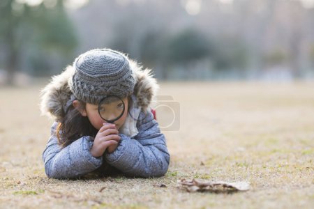 Téléchargez les photos : Petite fille dans un parc avec loupe à l'automne - en image libre de droit