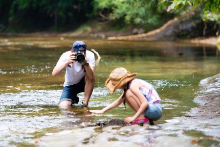 Téléchargez les photos : Père prenant une photo de sa fille jouant dans la rivière - en image libre de droit