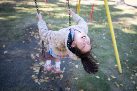 Foto de Asiático chica en swing en parque infantil en el parque - Imagen libre de derechos