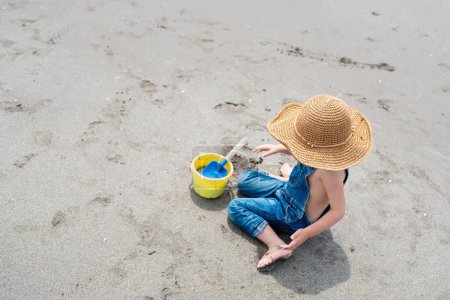 Foto de Hermosa pequeña asiática chica con juguetes se sienta en la playa - Imagen libre de derechos