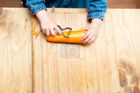 Téléchargez les photos : Mains d'un enfant qui épluche la carotte - en image libre de droit
