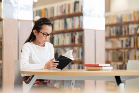 Téléchargez les photos : Jeune fille asiatique lecture livre dans la bibliothèque - en image libre de droit