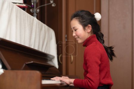 Foto de Joven asiático chica jugando piano en casa - Imagen libre de derechos