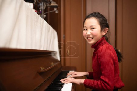 Photo for Young asian girl playing piano at home - Royalty Free Image