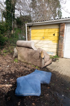 Un sillón de sofá abandonado y abandonado en los garajes volando bajo la lluvia