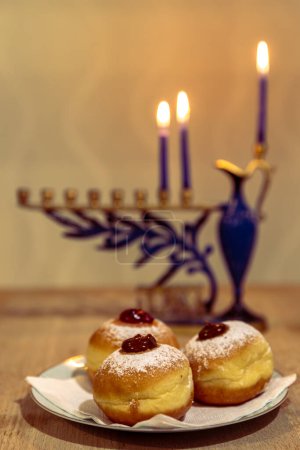 Photo for Menorah with lit burning candles for Jewish Hanukkah holiday on table at home. Celebrating Chanukah festival of lights.  Sufganiyot donuts sweet cultural food on a plate - Royalty Free Image