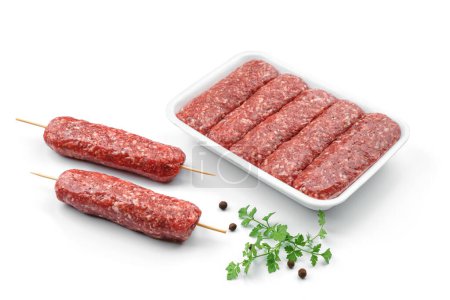 Foto de Embutidos de carne fresca en caserola con verduras y especias aisladas sobre fondo blanco. Comida de carne, vista superior - Imagen libre de derechos