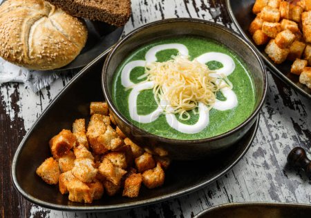 Photo for Vegan spinach soup with cheese, sour cream and croutons in bowl on rustic wooden background. Healthy food, top view - Royalty Free Image