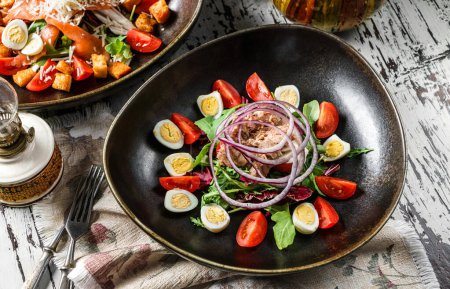 Foto de Ensalada de atún saludable con huevos, rúcula, tomates, lechuga en plato sobre fondo rústico de madera. Comida saludable, vista superior - Imagen libre de derechos