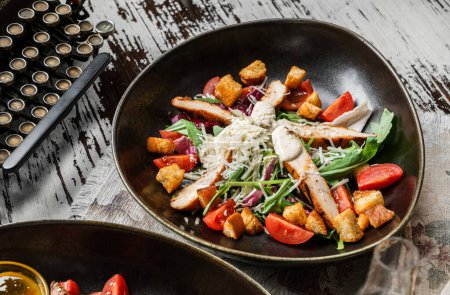 Foto de Ensalada de pollo saludable con croutons, rúcula, tomates, lechuga en plato sobre fondo rústico de madera. Comida saludable, vista superior - Imagen libre de derechos