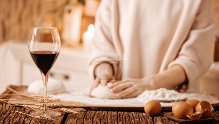 Téléchargez les photos : Verre de vin rouge sur table en bois avec épis de blé et coquilles d'oeuf sur le fond d'une femme qui cuisine, mise au point sélective - en image libre de droit