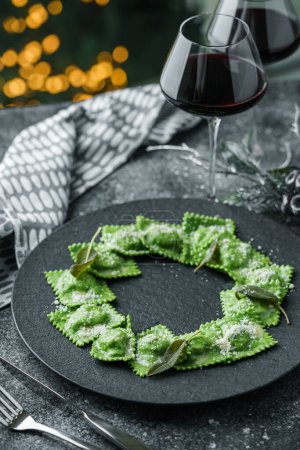 Photo for Green ravioli with spinach and ricotta cheese on plate over dark holiday background with glass of wine. Merry Christmas and New Year meal, vegetarian dishes, close up, bokeh - Royalty Free Image