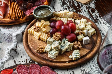 Photo for Cheese plate with parmesan, maasdam, blue cheese, brie cheese, cheddar with fruits and nuts on board over wooden background with glass of wine. Snacks and Wine appetizers set, top view - Royalty Free Image