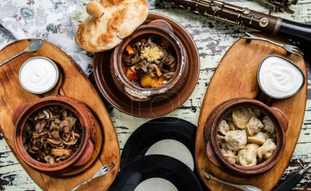 Photo for Homemade food, fried dumplings, baked potatoes with meat, baked mushrooms with onions in clay pot with sour cream on wooden board. Healthy food, top view - Royalty Free Image