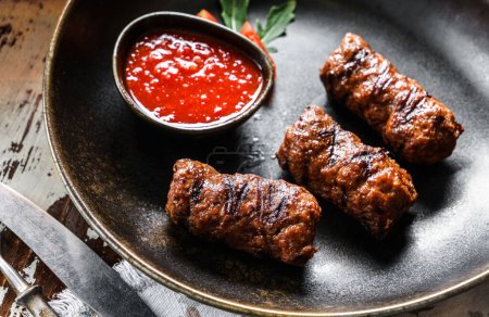 Téléchargez les photos : Saucisses de viande frites sur une assiette avec sauce tomate sur fond bois. Viande, gros plan - en image libre de droit