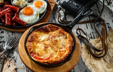 Foto de Delicioso desayuno, tortilla con verduras y queso servido en sartén caliente sobre fondo de madera. Comida saludable desayuno, primer plano - Imagen libre de derechos