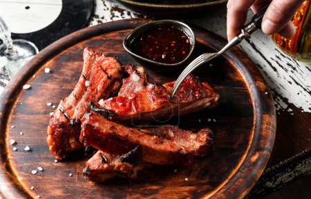 Photo for Hands cut barbecue pork spare ribs with hot honey chilli marinade on wooden cutting board with sauce on rustic background. Close up - Royalty Free Image