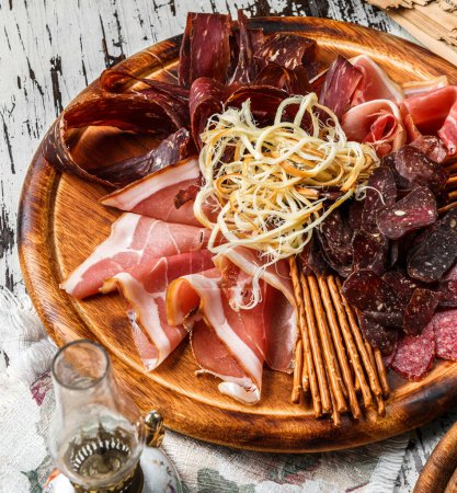 Photo for Antipasto cold meat platter with dry sausage, ham, salami, prosciutto, bacon decorated with smoked cheese, breadsticks on cutting board over wooden background. Meat snacks, beer set, top view - Royalty Free Image