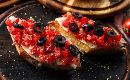 Foto de Bruschetta con pescado, pimiento, queso crema y aceitunas sobre pan de ciabatta sobre tabla de madera sobre fondo rústico. Comida sana, bocadillo de vino, primer plano - Imagen libre de derechos