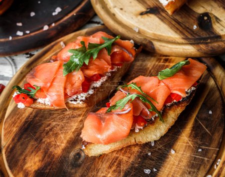 Photo for Bruschetta with salmon fish, bell pepper, cream cheese and arugula on ciabatta bread on wooden board over rustic background. Healthy food, sandwich of wine, close up - Royalty Free Image