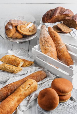 Photo for Assortment of various delicious freshly baked bread on white wooden background. Vertuta, stuffed bread, pastries, croissants, strudel, baguette, buns. Homemade healthy bread, grocery store, top view - Royalty Free Image