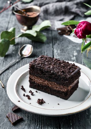 Téléchargez les photos : Pièce de gâteau brownie au chocolat avec des pépites de chocolat dans une assiette sur fond sombre avec des fleurs de pivoine. Bonbons, dessert et pâtisserie, vue sur le dessus - en image libre de droit