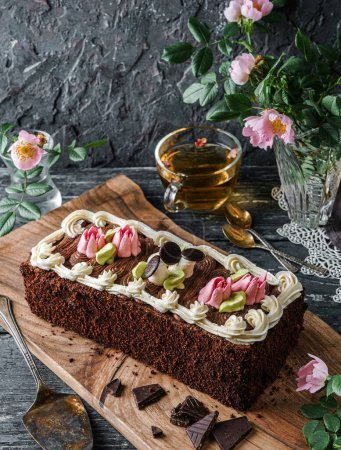 Photo for Delicious biscuit cake "Fairy Tale" decorated with dessert mushrooms and flowers with chocolate cream on dark background with cup of tea and spring flowers. Sweets, dessert and pastry, top view - Royalty Free Image