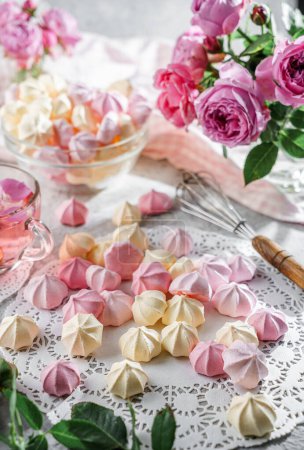 Photo for Pastel coloured meringues, zephyr, on lace napkin with cup of tea and rose flowers on light background. Sweets, dessert and pastry, homemade cakes, top view, selective focus - Royalty Free Image