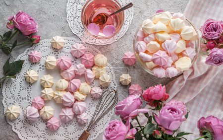 Foto de Merengues de color pastel, zephyr, en servilleta de encaje con taza de té y flores de rosas sobre fondo claro. Dulces, postres y pasteles, pasteles caseros, vista superior - Imagen libre de derechos