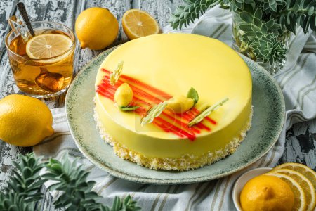 Téléchargez les photos : Gâteau en mousse jaune avec glaçure miroir, limons sur fond bois clair avec tasse de thé et de plantes. Bonbons, dessert et pâtisserie, vue sur le dessus - en image libre de droit