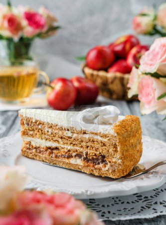 Photo for Piece of delicious cake with cream and apple jam on the plate over grey background with fresh apples and flowers. Sweets, dessert and pastry, close up, selective focus - Royalty Free Image