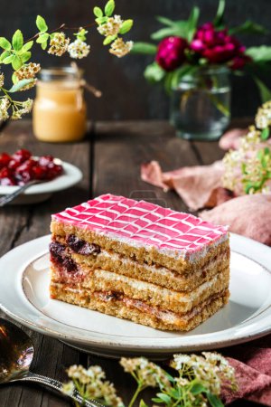 Photo for Piece of delicious biscuit cake with cherry and condensed milk on the plate over dark wooden background with berries and flowers. Sweets, dessert and pastry, homemade cakes, close up, selective focus - Royalty Free Image