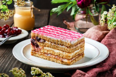 Photo for Piece of delicious biscuit cake with cherry and condensed milk on the plate over dark wooden background with berries and flowers. Sweets, dessert and pastry, homemade cakes, close up, selective focus - Royalty Free Image