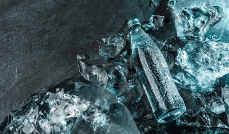 Foto de Botella de agua en hielo sobre fondo de piedra. Piezas de hielo iluminadas con luz azul. Publicidad de agua mineral en botella de vidrio, vista superior - Imagen libre de derechos