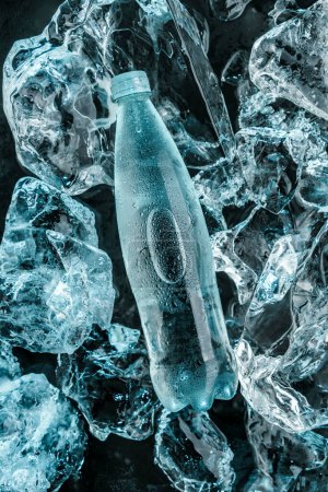 Foto de Botella de agua en hielo. Piezas de hielo iluminadas con luz azul. Publicidad de agua mineral en botella de vidrio, vista superior - Imagen libre de derechos