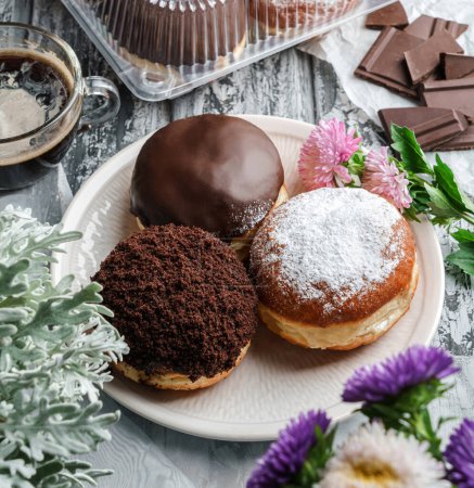 Photo for Yummy set of cake donuts with vanilla, chocolate icing, powdered sugar and chocolate chips on plate on grey background with flowers. Sweets, dessert and pastry, top view, close up - Royalty Free Image