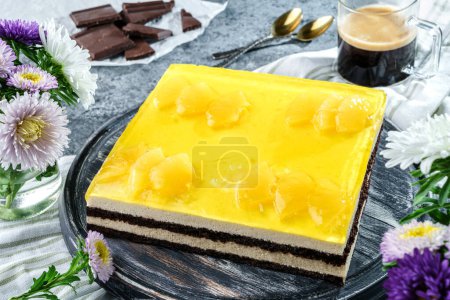Téléchargez les photos : Gâteau en mousse jaune avec gelée d'ananas sur fond gris avec tasse de café, chocolat et fleurs. Bonbons, dessert et pâtisserie, vue sur le dessus - en image libre de droit