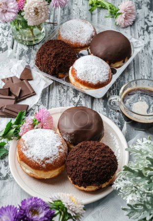 Photo for Yummy set of cake donuts with vanilla, chocolate icing, powdered sugar and chocolate chips on plate on grey background with flowers. Sweets, dessert and pastry, top view, close up - Royalty Free Image