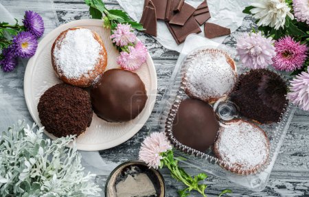 Photo for Yummy set of cake donuts with vanilla, chocolate icing, powdered sugar and chocolate chips on plate on grey background with flowers. Sweets, dessert and pastry, top view - Royalty Free Image
