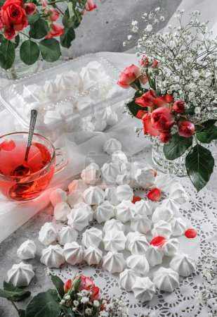 Foto de Merengues blancos, zephyr, en servilleta de encaje con taza de té y flores de rosas sobre fondo claro. Dulces, postres y pasteles, pasteles caseros, vista superior, enfoque selectivo - Imagen libre de derechos