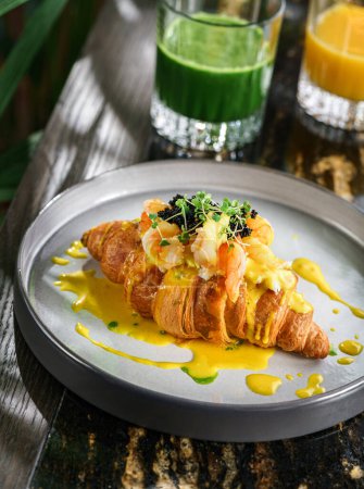 Photo for Delicious croissant with egg benedict or poached egg, black caviar, shrimps and microgreens on plate on marble table with smoothies. Healthy breakfast food, diet, top view - Royalty Free Image