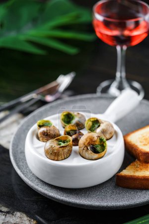 Foto de Deliciosos caracoles marinos con hierbas en plato sobre fondo de mármol con bebidas. Comida gourmet. Escargot Caracoles, vista superior - Imagen libre de derechos