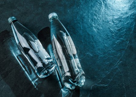 Téléchargez les photos : Deux bouteilles d'eau sur fond de pierre sombre. Publicité eau minérale en bouteille en verre, vue de dessus - en image libre de droit