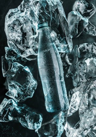 Foto de Botella de agua en hielo. Piezas de hielo iluminadas con luz azul. Publicidad de agua mineral en botella de vidrio, vista superior - Imagen libre de derechos